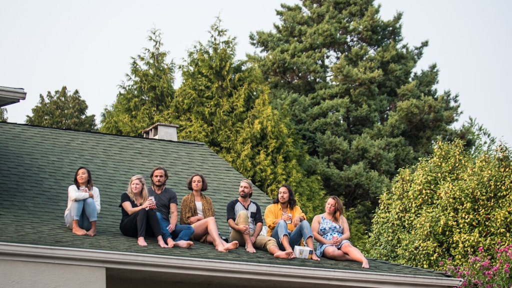 A group of people sit in a line on a green rooftop, watching a Sofar show